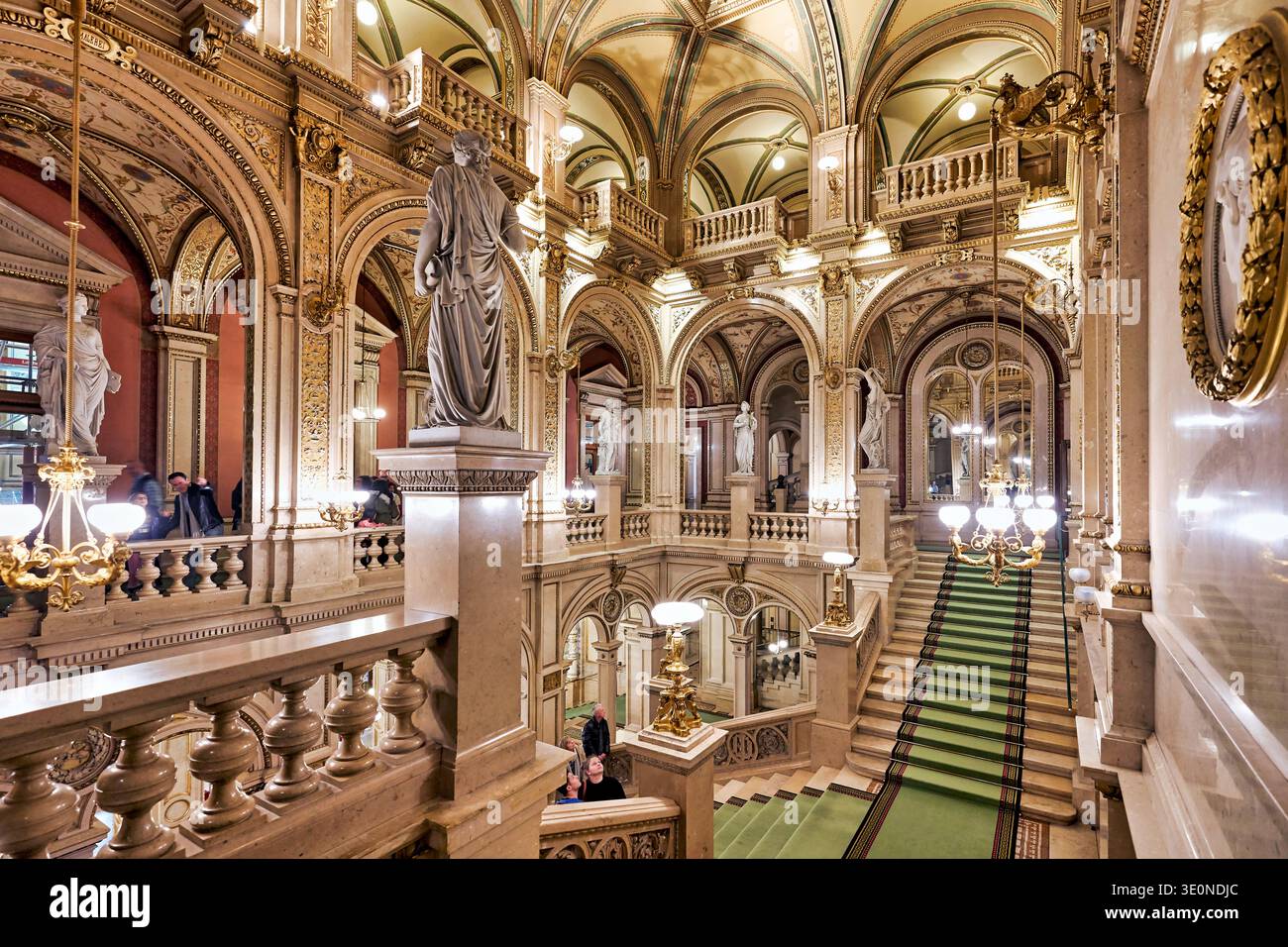 Les touristes se promènent dans l'Opéra national de Vienne, admirant le grand escalier, les statues et les détails dorés de son intérieur. Banque D'Images