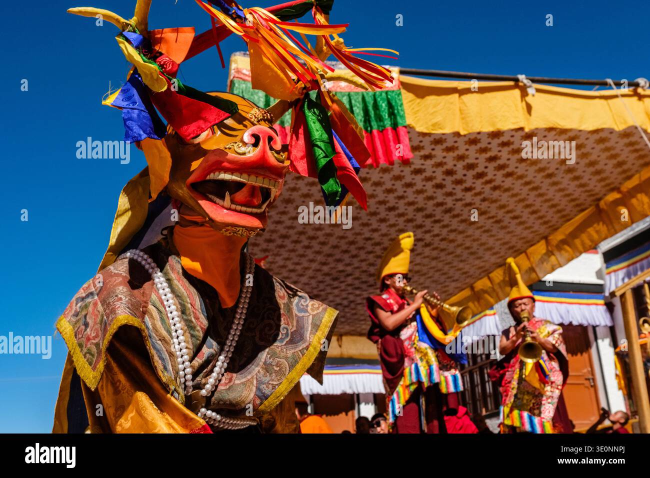 Un danseur dans un masque à tête animale se produit tandis que des moines de l'ordre du chapeau jaune jouent des instruments à vent traditionnels au Diskit Gustor. Banque D'Images