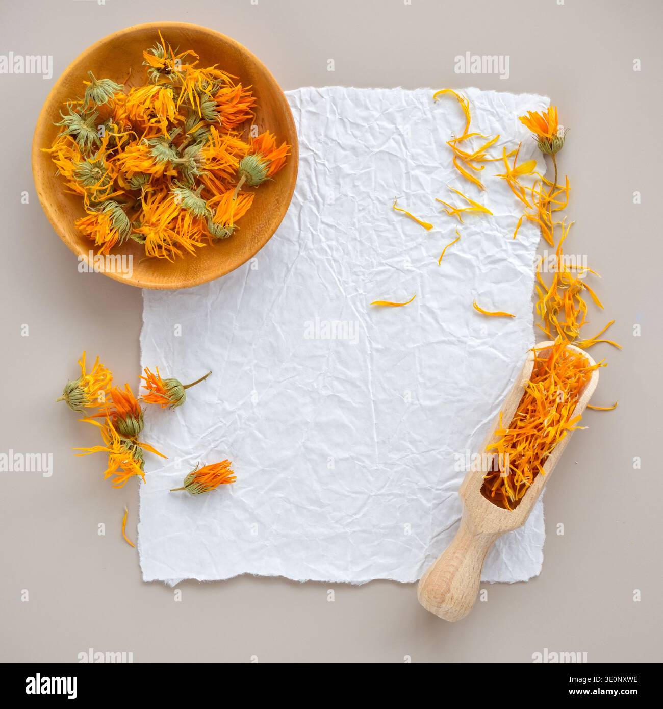 Fleurs séchées de calendula dans un bol en bois et une pétales en bois avec des pétales sur papier texturé. Vue de dessus avec espace pour le texte Banque D'Images