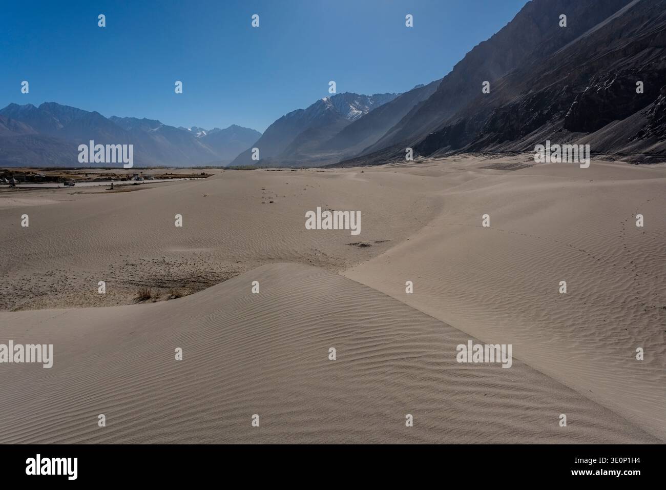 Les dunes de sable ondulantes de Hunder s'étendent à travers le fond de la vallée vers les sommets brumeux de la chaîne de Karakoram visibles au loin. Banque D'Images