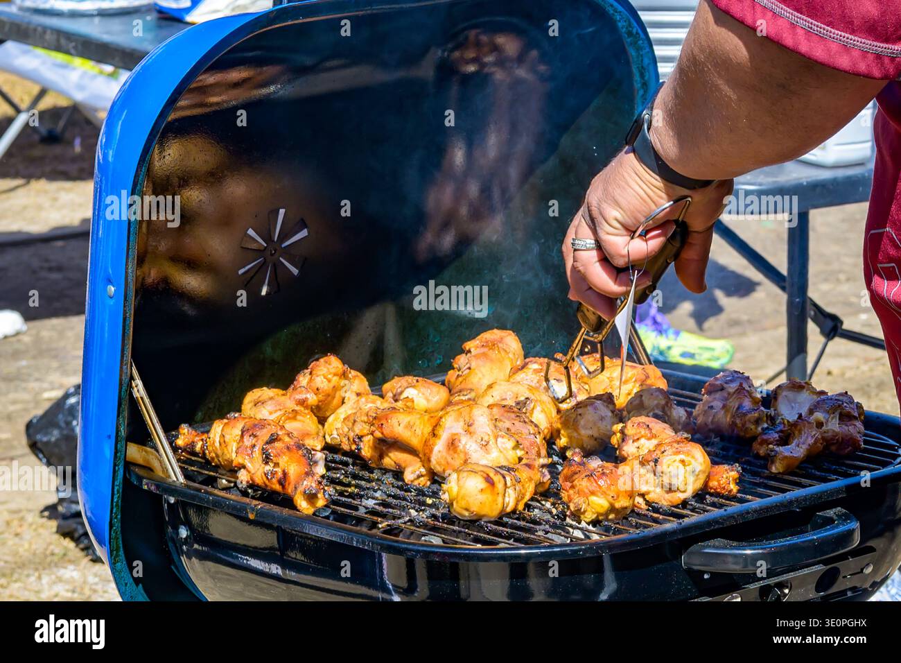 Gros plan de la main d'un homme tenant des pinces cuisant des pilons de poulet sur un barbecue à l'extérieur sur la route de la parade Uptown mardi gras à la Nouvelle-Orléans, LA, États-Unis le 13 février 2024 à la Nouvelle-Orléans, LA, États-Unis Banque D'Images