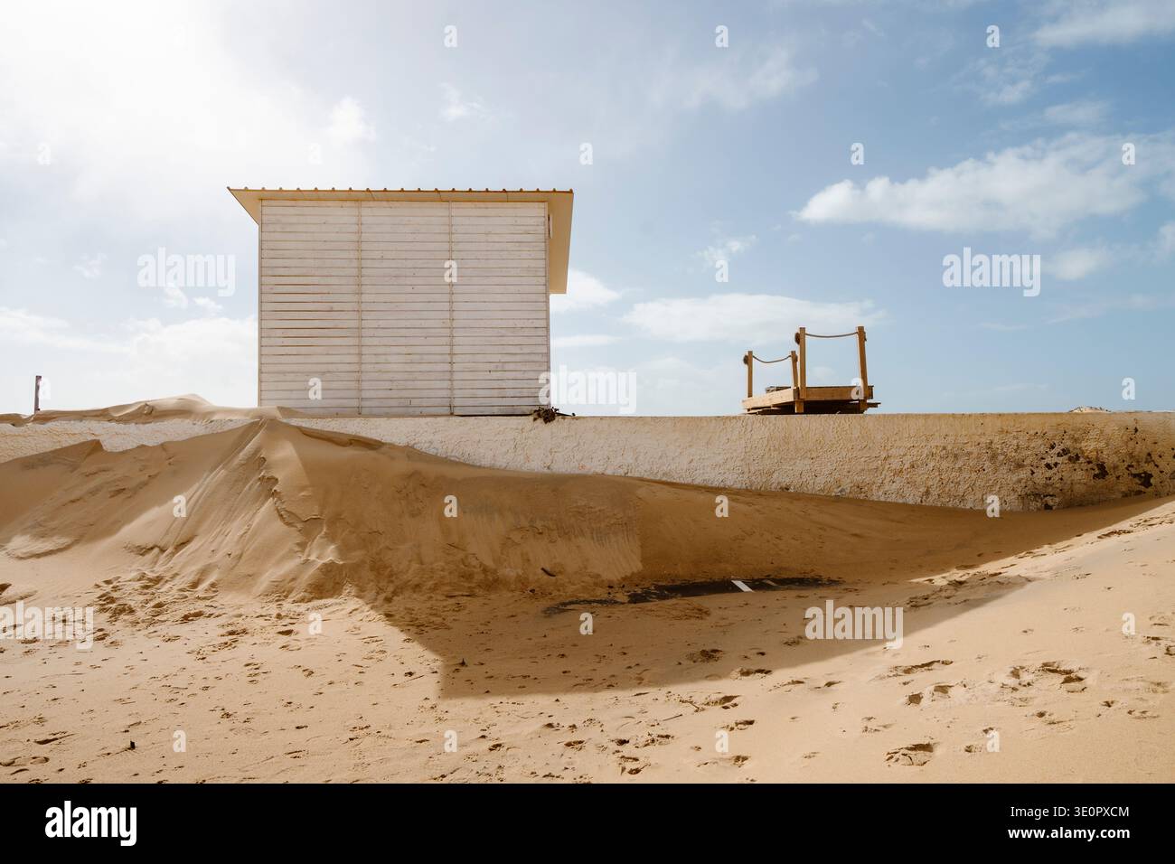 Petite cabane de plage en bois blanc debout à côté d'énormes dérives de sable formées après de puissantes tempêtes d'hiver de l'Atlantique sur la plage de Faro en Algarve, Portugal. Larg Banque D'Images