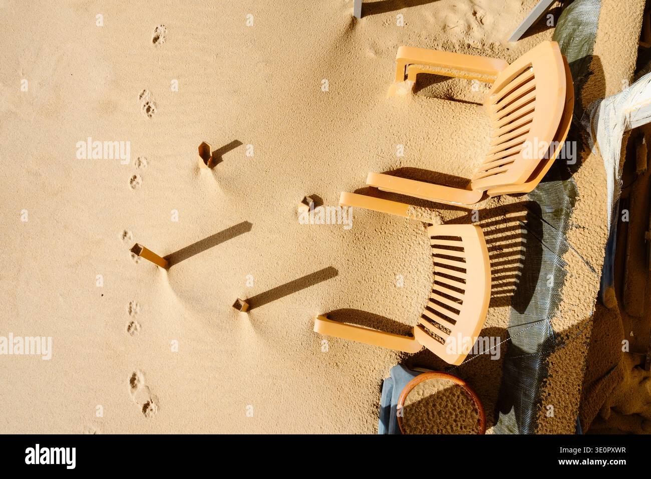 Une scène côtière minimaliste sur la plage de Faro, Algarve, Portugal, montrant des chaises en plastique partiellement enterrées dans le sable après les tempêtes hivernales. Certaines chaises restent U. Banque D'Images