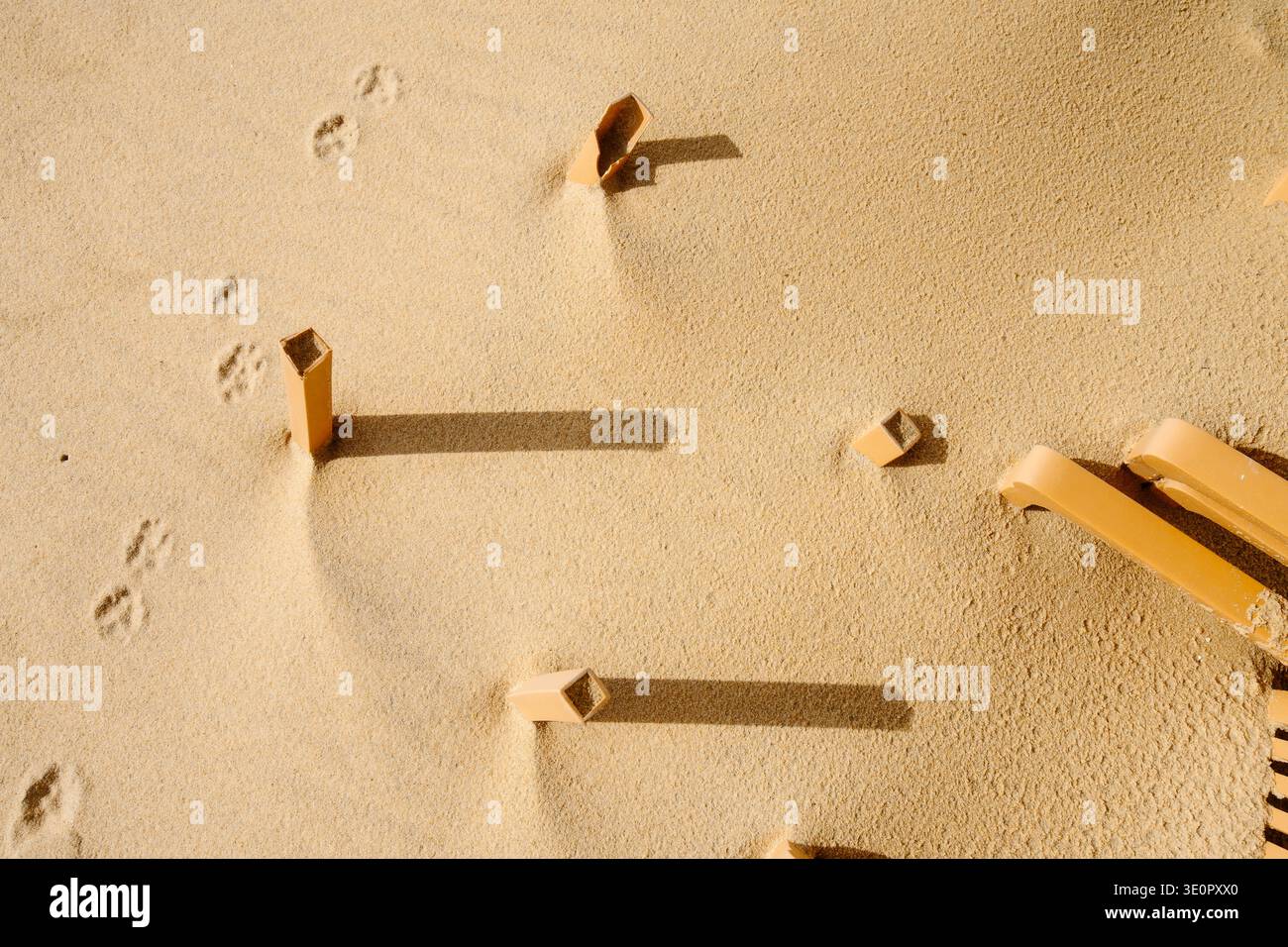 Une scène côtière minimaliste sur la plage de Faro, Algarve, Portugal, montrant des chaises en plastique partiellement enterrées dans le sable après les tempêtes hivernales. Certaines chaises restent U. Banque D'Images