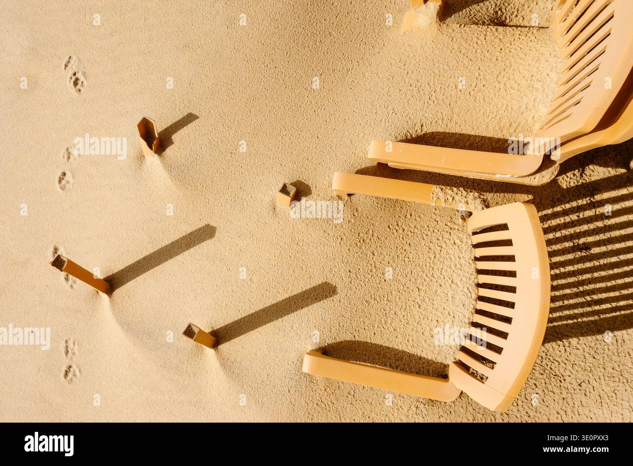 Une scène côtière minimaliste sur la plage de Faro, Algarve, Portugal, montrant des chaises en plastique partiellement enterrées dans le sable après les tempêtes hivernales. Certaines chaises restent U. Banque D'Images