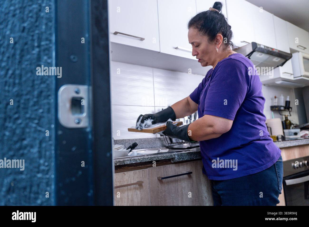 Femme debout à un évier de cuisine moderne nettoyant une planche à découper et faisant les tâches ménagères Banque D'Images