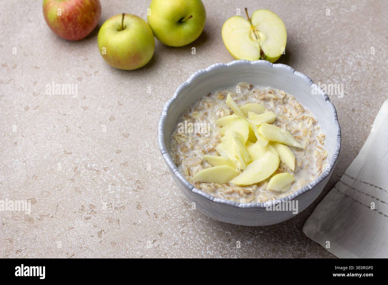 Bouillie d'avoine au lait garnie de tranches de pommes fraîches dans un bol en céramique. Petit déjeuner nutritif avec avoine et fruits sur la table de cuisine légère Banque D'Images