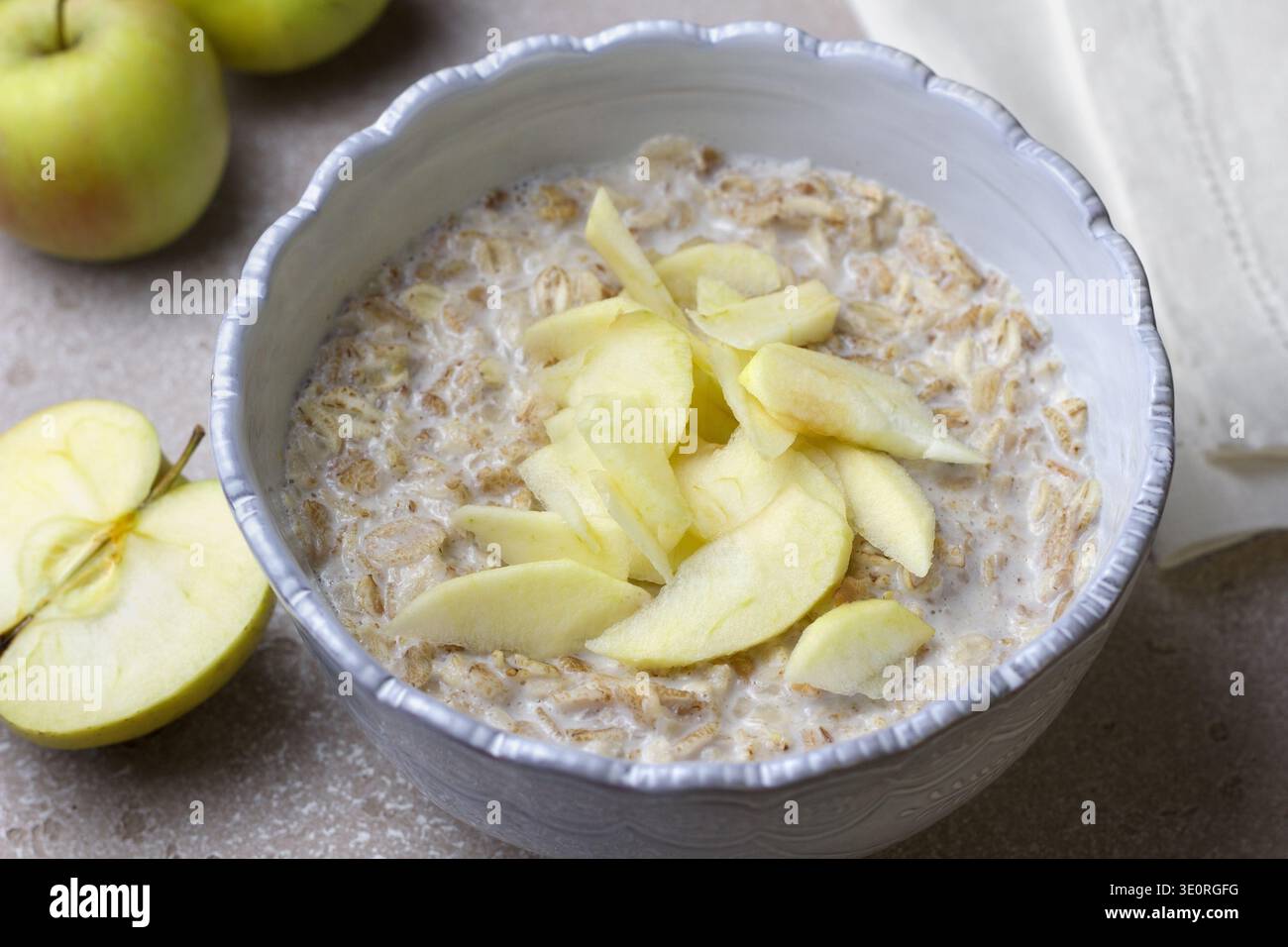 Bouillie d'avoine au lait garnie de tranches de pommes fraîches dans un bol en céramique. Petit déjeuner nutritif avec avoine et fruits sur la table de cuisine légère Banque D'Images