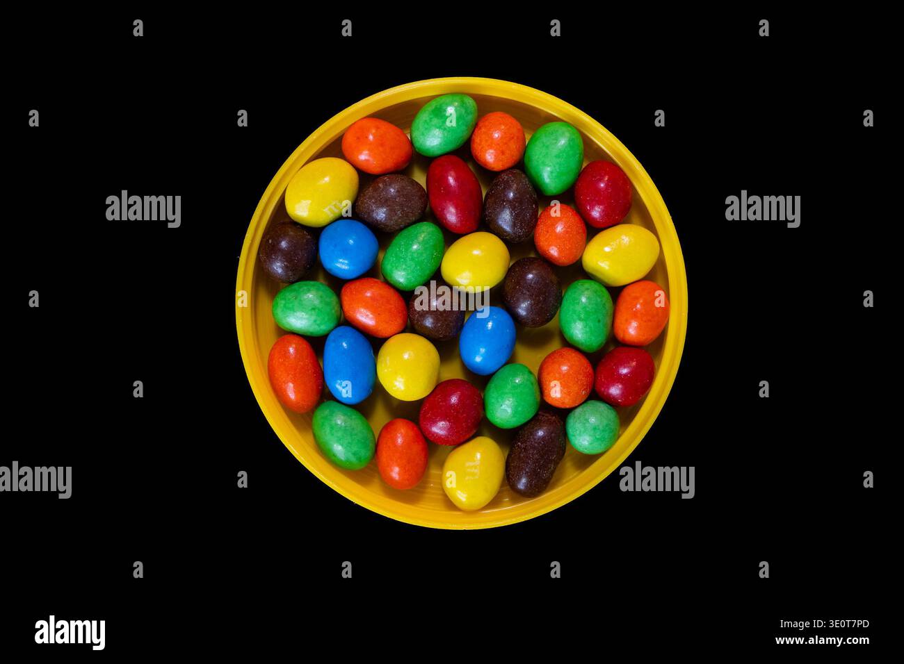 Bonbons au chocolat multicolores dans un bol jaune sur fond noir Banque D'Images