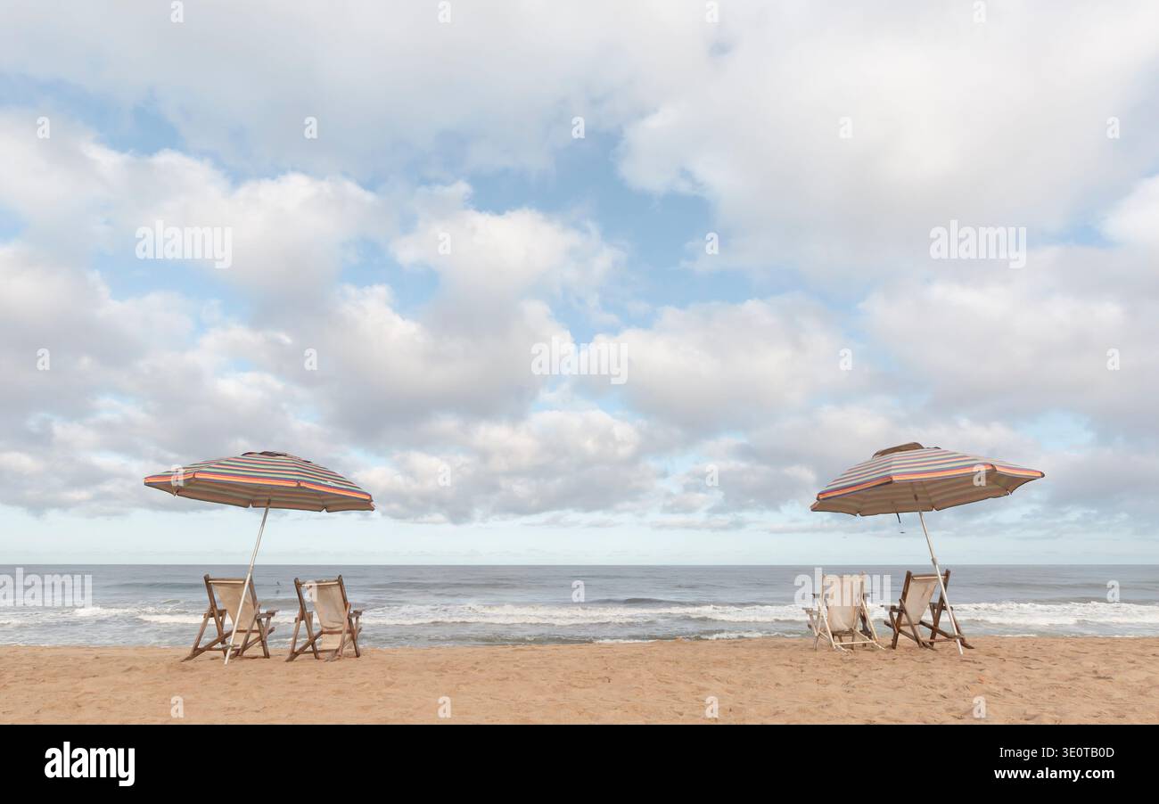 Deux parasols de plage rayés avec des chaises longues vides face à l'océan sous un ciel nuageux dramatique, San Pancho, Nayarit, Mexique Banque D'Images