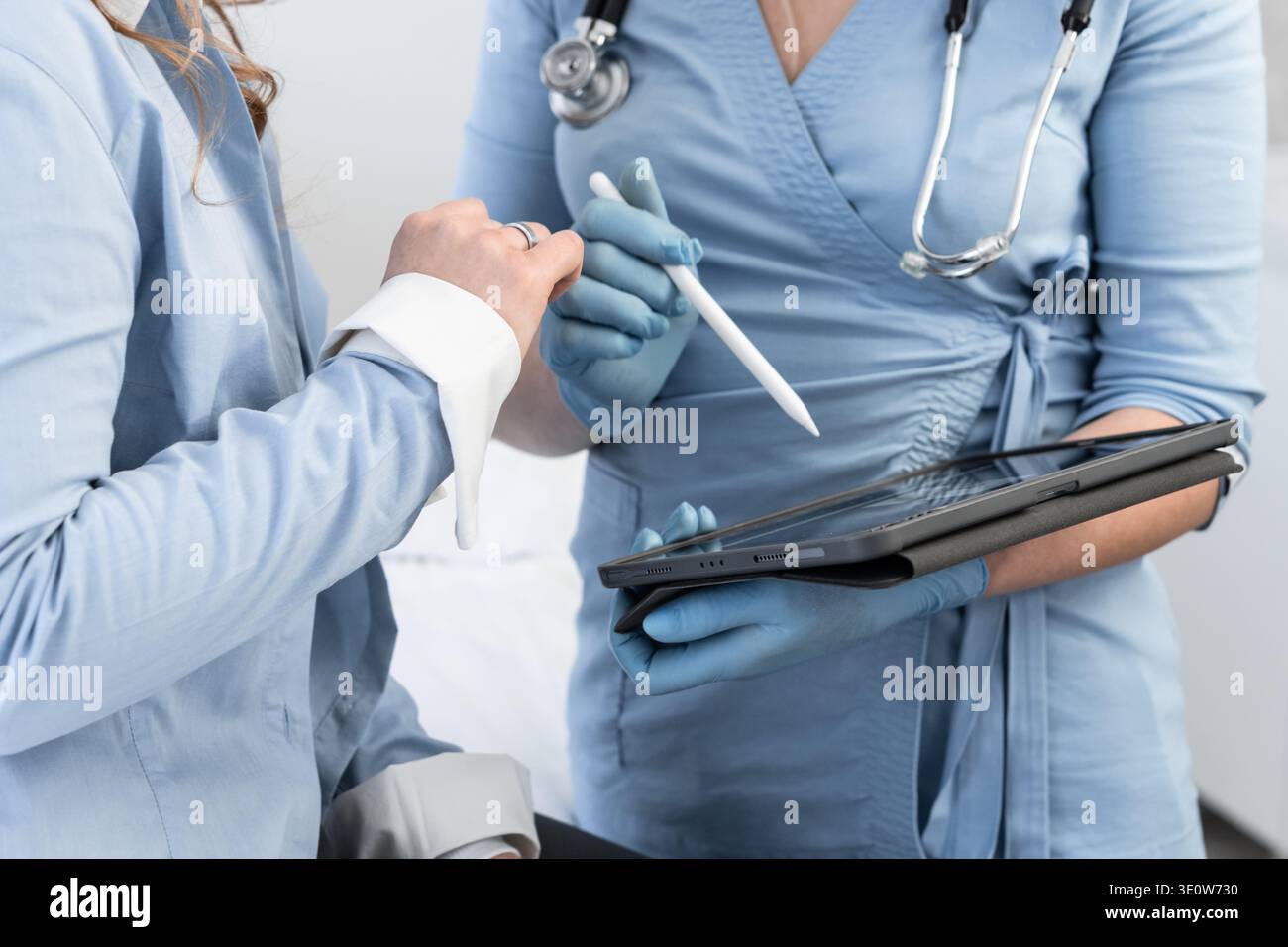Les médecins en tenue médicale discutent des informations sur le patient tout en interagissant avec une tablette tactile et un stylet. Les outils numériques rationalisent la communication dans le domaine de la santé et améliorent l'efficacité Banque D'Images