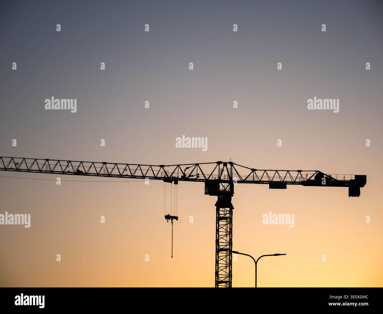 Silhouette de grue à tour contre ciel de coucher de soleil dégradé avec crochet suspendu et lampadaire en Estonie, mars 2026 Banque D'Images