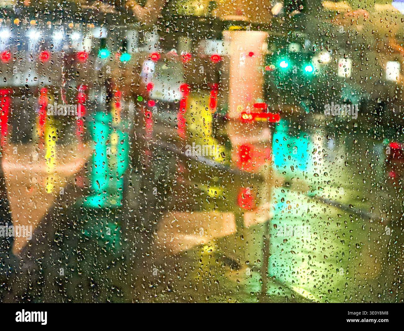 Gouttes de pluie sur une fenêtre rétroéclairée par les lumières des bâtiments et des feux de circulation - Image de stock capturée avec un smartphone