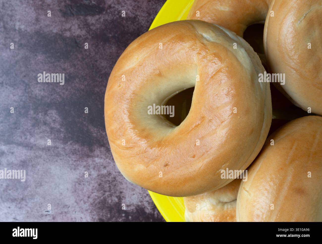 Vue de dessus d'un groupe de bagels simples sur une grande plaque jaune au sommet d'une table marbrée rouge illuminée d'un éclairage naturel. Banque D'Images
