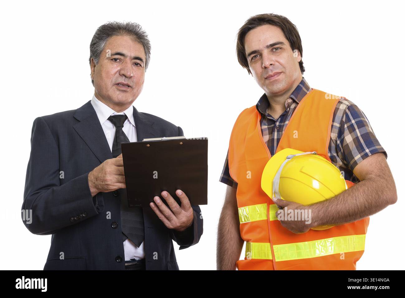 Studio shot of Persian senior businessman holding clipboard avec jeune homme persan construction worker Banque D'Images