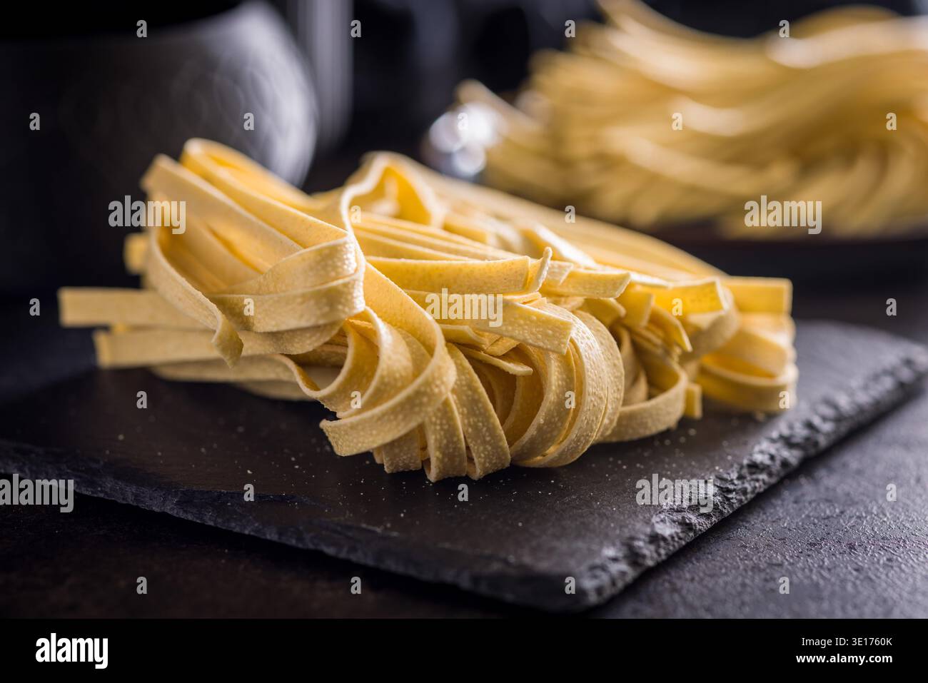 Les brins de pâtes fettuccine reposent sur une surface blanche, paraissant doux et frais. Ce type de pâtes est souvent utilisé dans divers plats. Banque D'Images