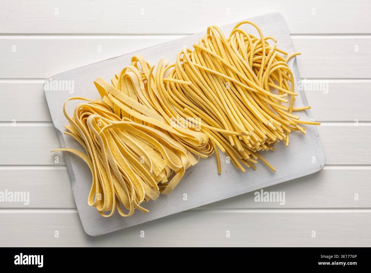 Des brins de fettuccine et de bigoli reposent sur une surface blanche, paraissant doux et frais. Ce type de pâtes est souvent utilisé dans divers plats. Banque D'Images