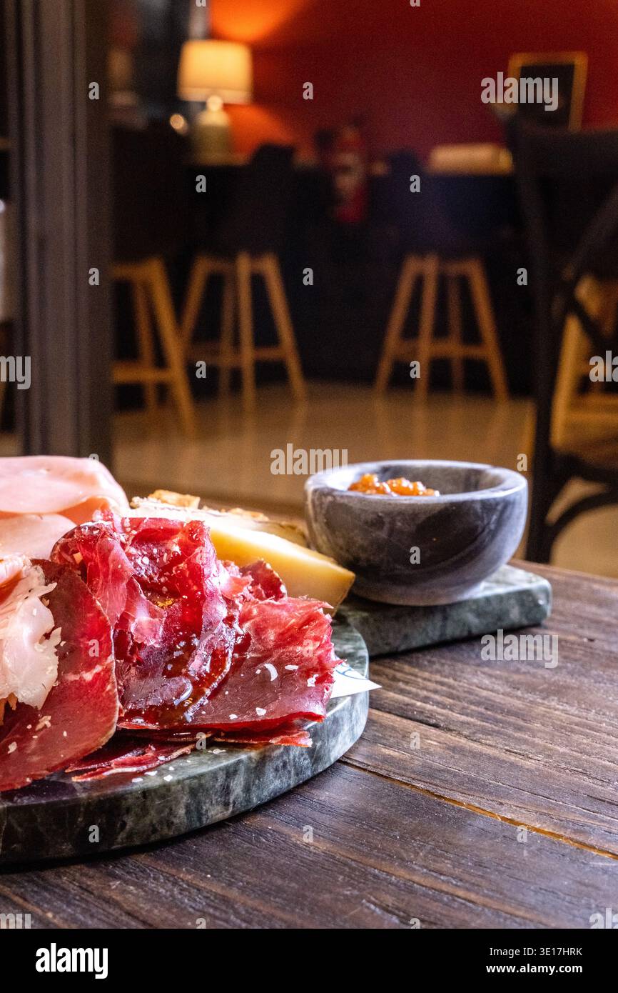 Gros plan d'un plateau de charcuterie avec des tranches de jambon salé, disposées avec du fromage sur un plateau de pierre. Un éclairage ambiant chaud améliore la richesse Banque D'Images