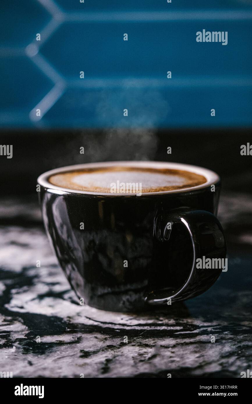 Gros plan d'une tasse de café noir fumant placée sur une surface en marbre richement texturée. Les tons sombres de la tasse contrastent élégamment avec le dos sombre Banque D'Images