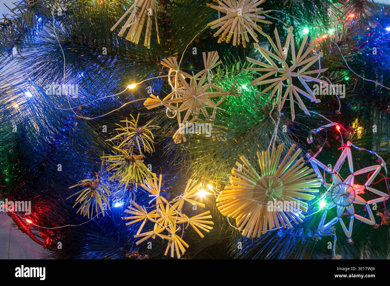 Ornements de Noël en paille sur arbre. Décorations rustiques sur l'arbre de Noël. Guirlande lumineuse multicolore Banque D'Images