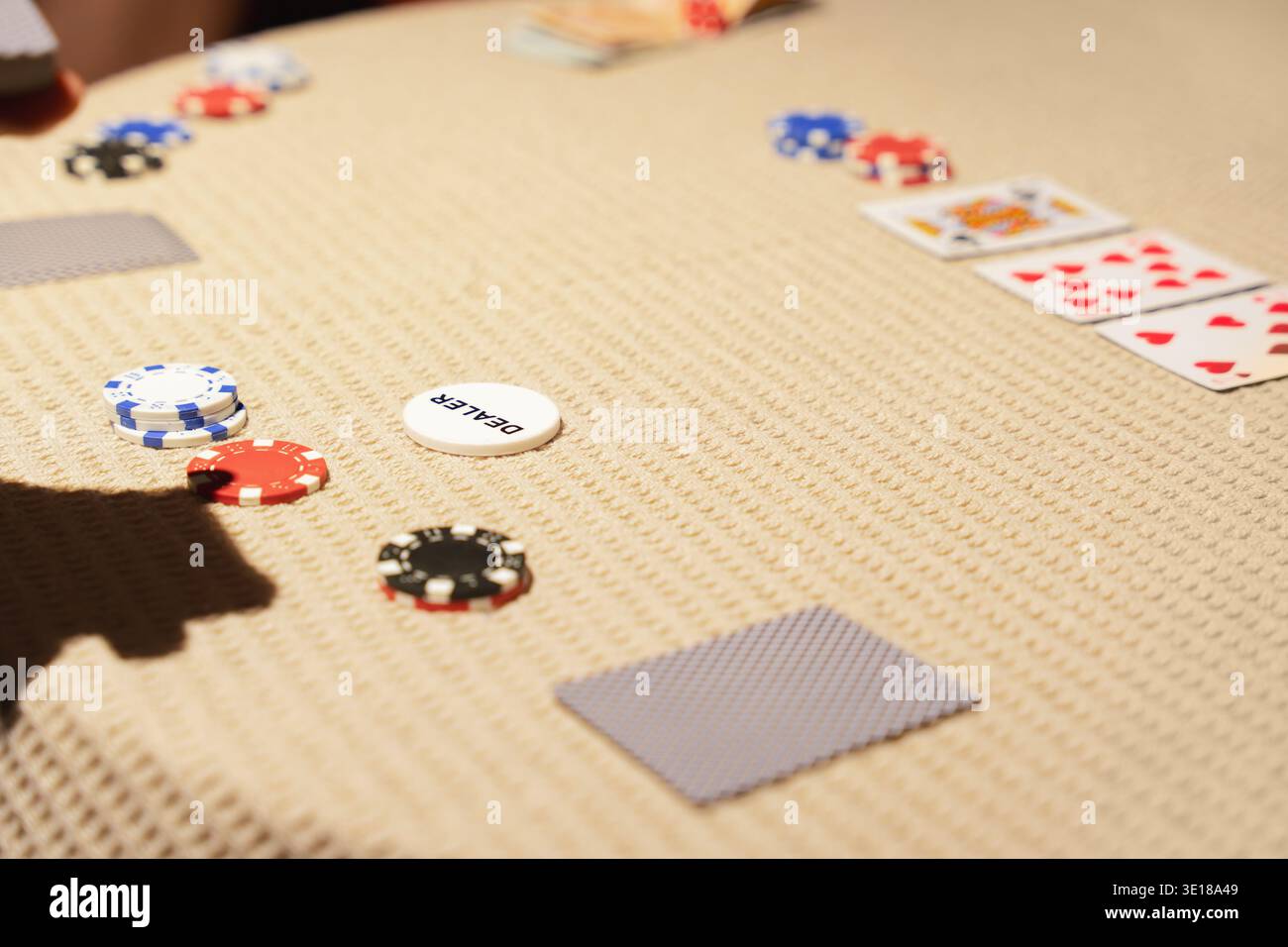 Jetons de poker et cartes à jouer dispersés sur la table texturée avec bouton de croupier pendant le jeu de cartes de casino, jeu domestique Banque D'Images