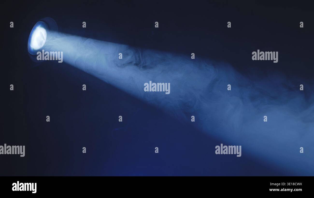 Faisceau de spot bleu brillant à travers une fumée dense sur une scène sombre. Effet d'éclairage théâtral. Banque D'Images