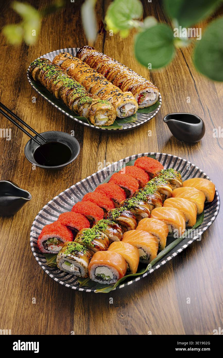 De délicieux rouleaux de sushi sont agencés avec art sur deux assiettes, présentant une variété de couleurs et de textures. Un plat de sauce soja et des baguettes sont placés Alo Banque D'Images