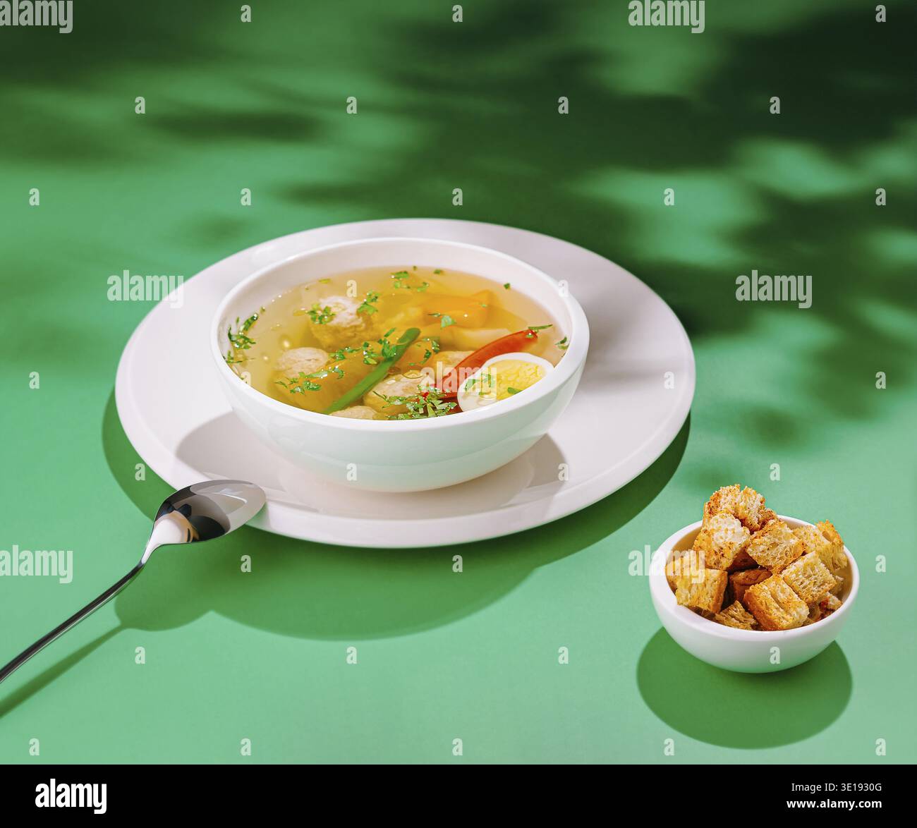Soupe de poulet à la vapeur avec boulettes de viande, légumes et herbes servies avec des croûtons sur fond vert Banque D'Images
