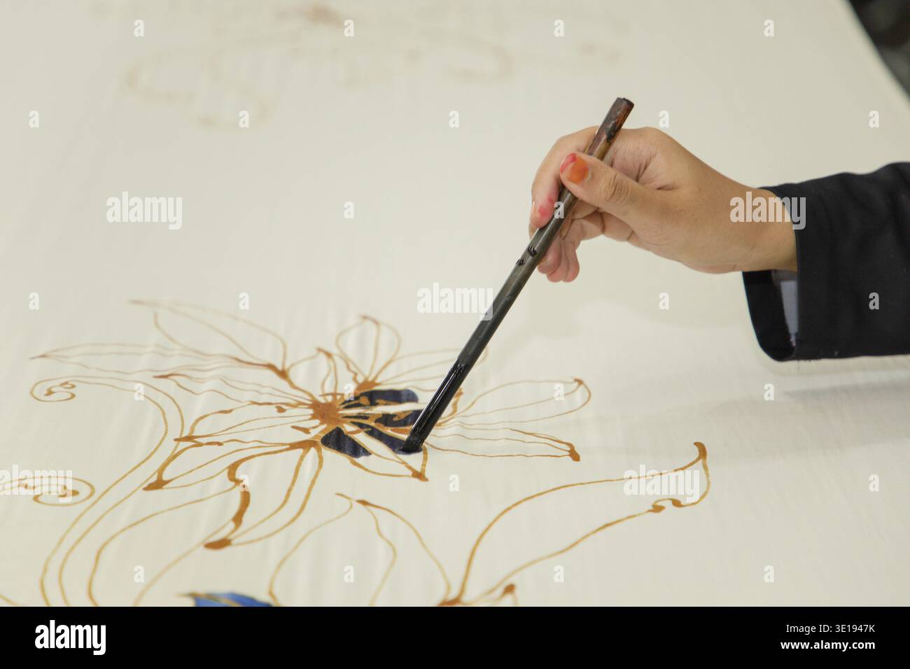 Gros plan main de femme avec pinceau peinture Batik sur tissu de batik malaisien Banque D'Images