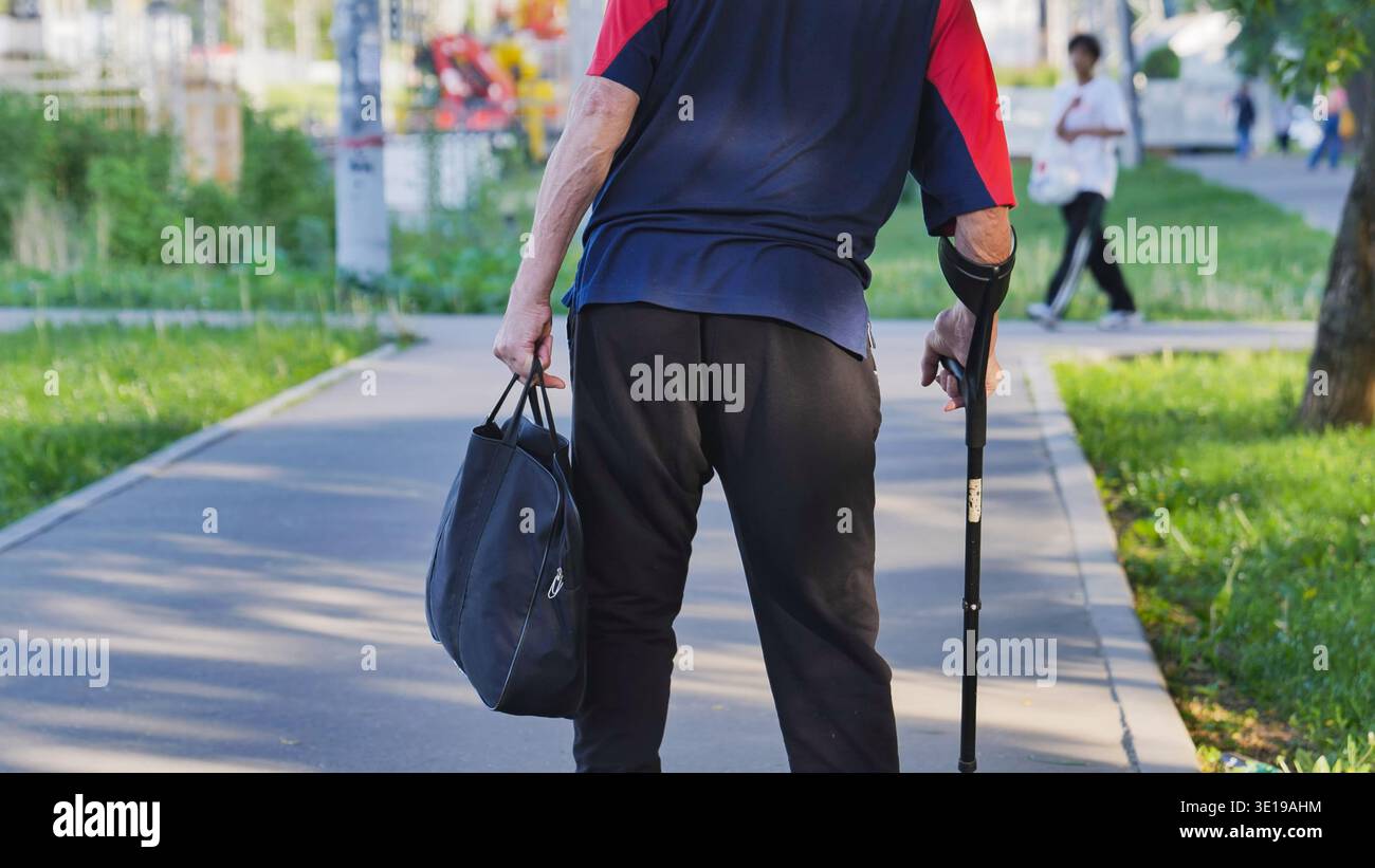 Homme âgé marchant avec béquille d'avant-bras et sac à travers le parc urbain à Moscou Banque D'Images