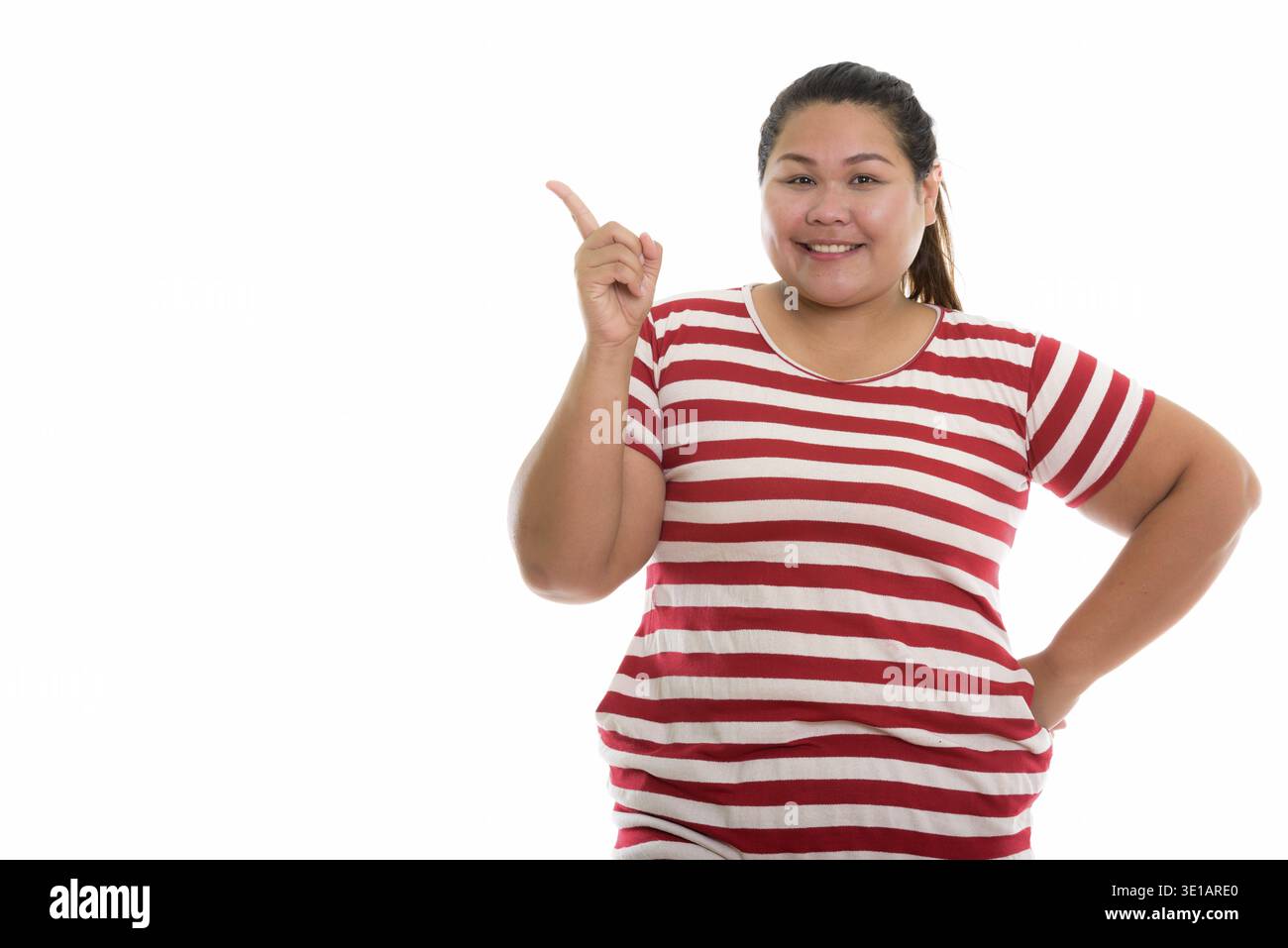 Studio shot of young happy fat woman smiling while pointing finger up Banque D'Images
