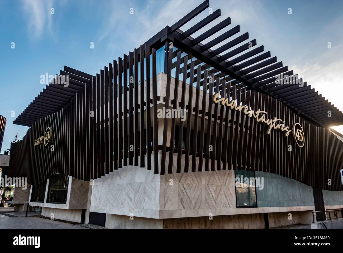 Extérieur de Cuarentaytrés à Cartagena, Espagne. Architecture moderne avec une façade en pierre, des lattes verticales sombres et une signalisation dorée sous un ciel bleu. Banque D'Images