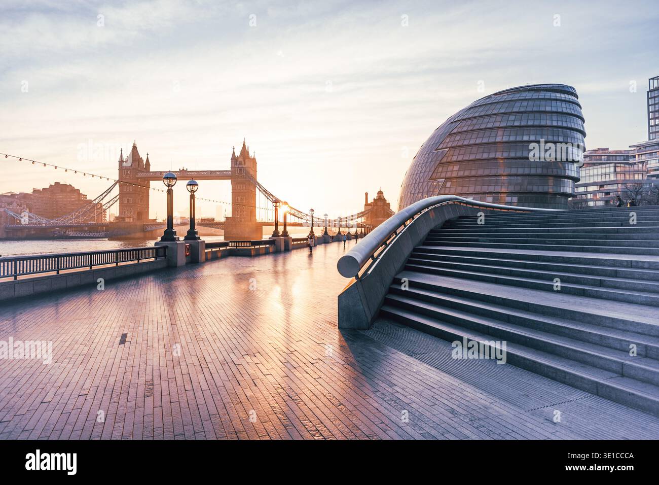 Le soleil du matin baigne Tower Bridge dans des teintes dorées, vues depuis le Queen's Walk à Londres. L'atmosphère tranquille est renforcée par la rivière calme et l'architecture moderne à proximité. Banque D'Images
