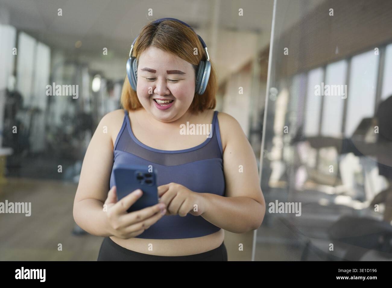 Femme avec téléphone intelligent après l'entraînement à Gym. Femme asiatique obèse regardant la classe de formation d'entraînement en ligne Banque D'Images