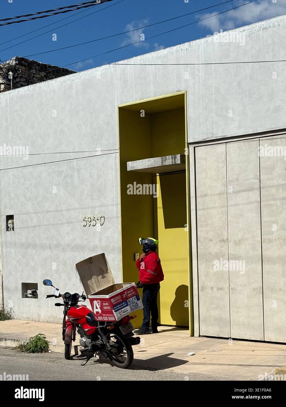 Pilote de livraison de nourriture sur une moto devant une maison à Mérida, Yucatán, Mexique Banque D'Images