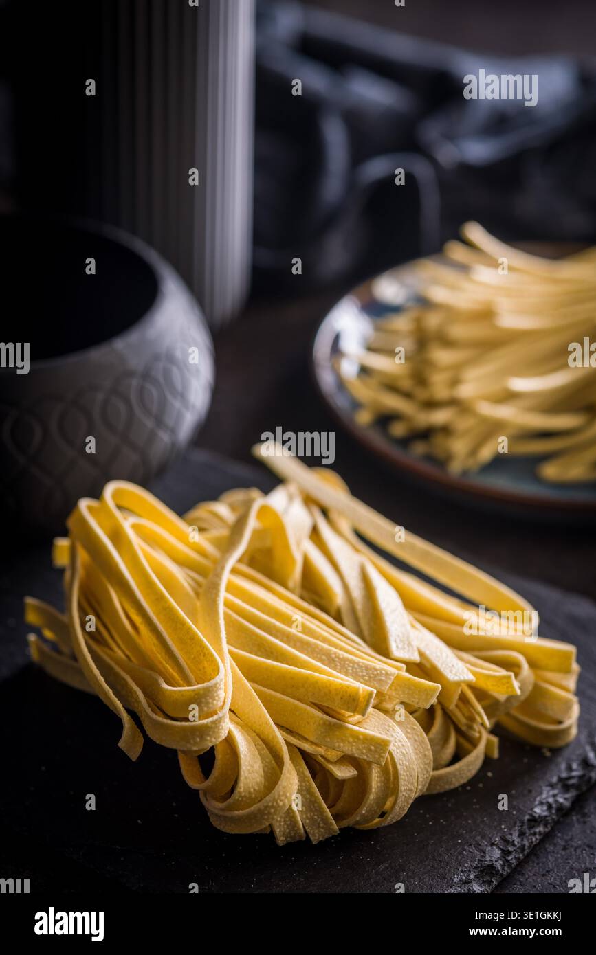 Les brins de pâtes fettuccine reposent sur une surface blanche, paraissant doux et frais. Ce type de pâtes est souvent utilisé dans divers plats. Banque D'Images
