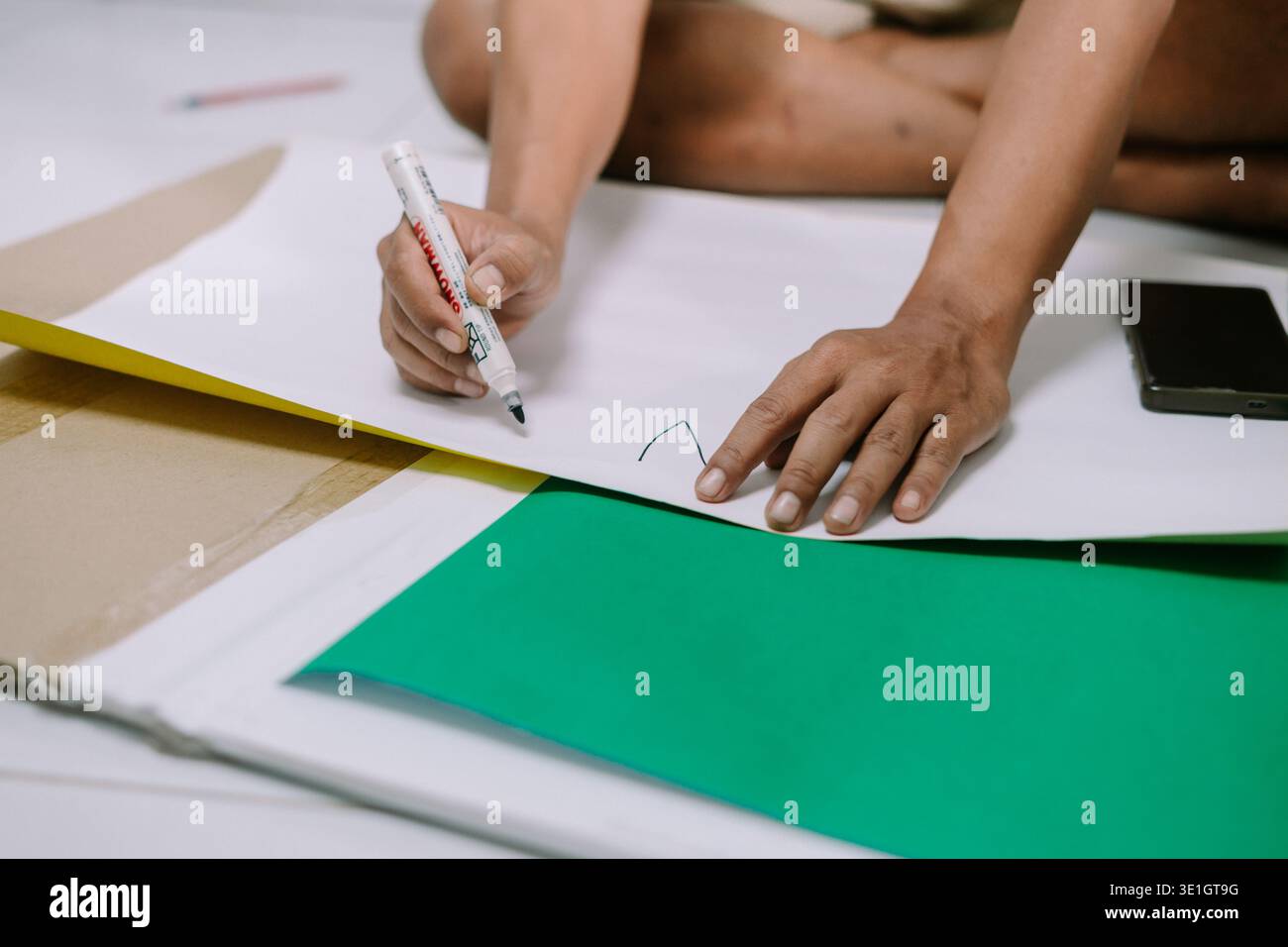 Gros plan de mains dessinant un dessin simple sur papier blanc avec un marqueur, illustrant un processus créatif ou un passe-temps. Les matériaux artisanaux comme le papier vert le sont Banque D'Images
