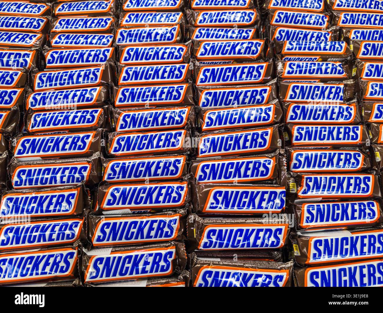 Pile massive de tablettes de chocolat Snickers enveloppées dans un emballage brun et bleu disposé dans une texture solide plate à Sokuluk, Kirghizistan - 18 juin 2024 Banque D'Images