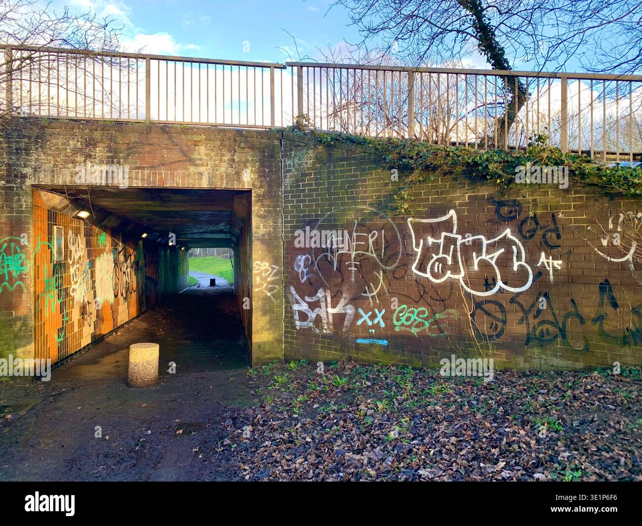 Le passage souterrain piétonnier couvert de graffitis se trouve en dessous du pont routier A43 Northampton et de l'art de rue sur les murs de briques et les feuilles tombées de la surface intérieure - Image de stock capturée avec un smartphone