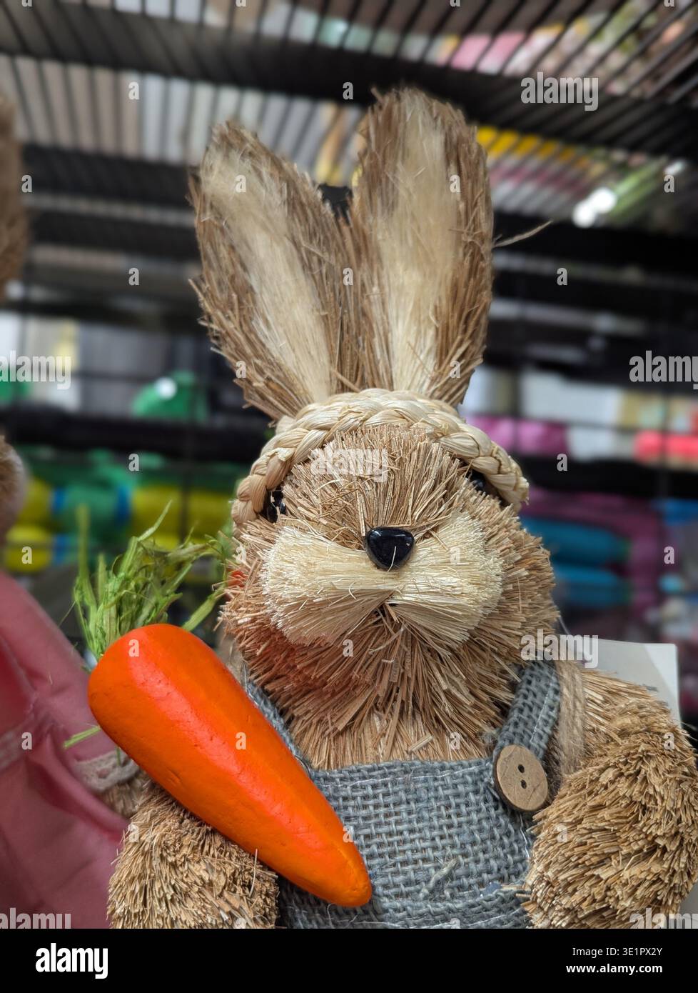 Lapin de paille tenant carotte brillante, pull tricoté avec détail de bouton, affichage de marché rustique sur l'étagère offrant une vibe de Pâques de ferme ludique avec la main Banque D'Images