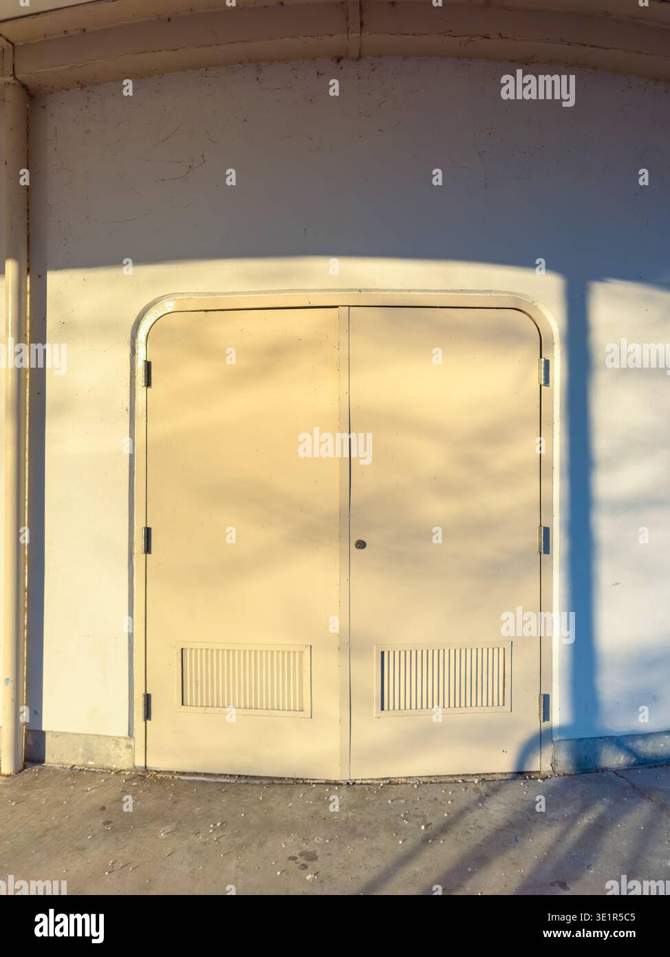 Deux portes sont installées dans un mur lumineux. Le soleil est bas, faisant de longues ombres sur le sol. La scène montre une zone simple sans personne autour. Banque D'Images