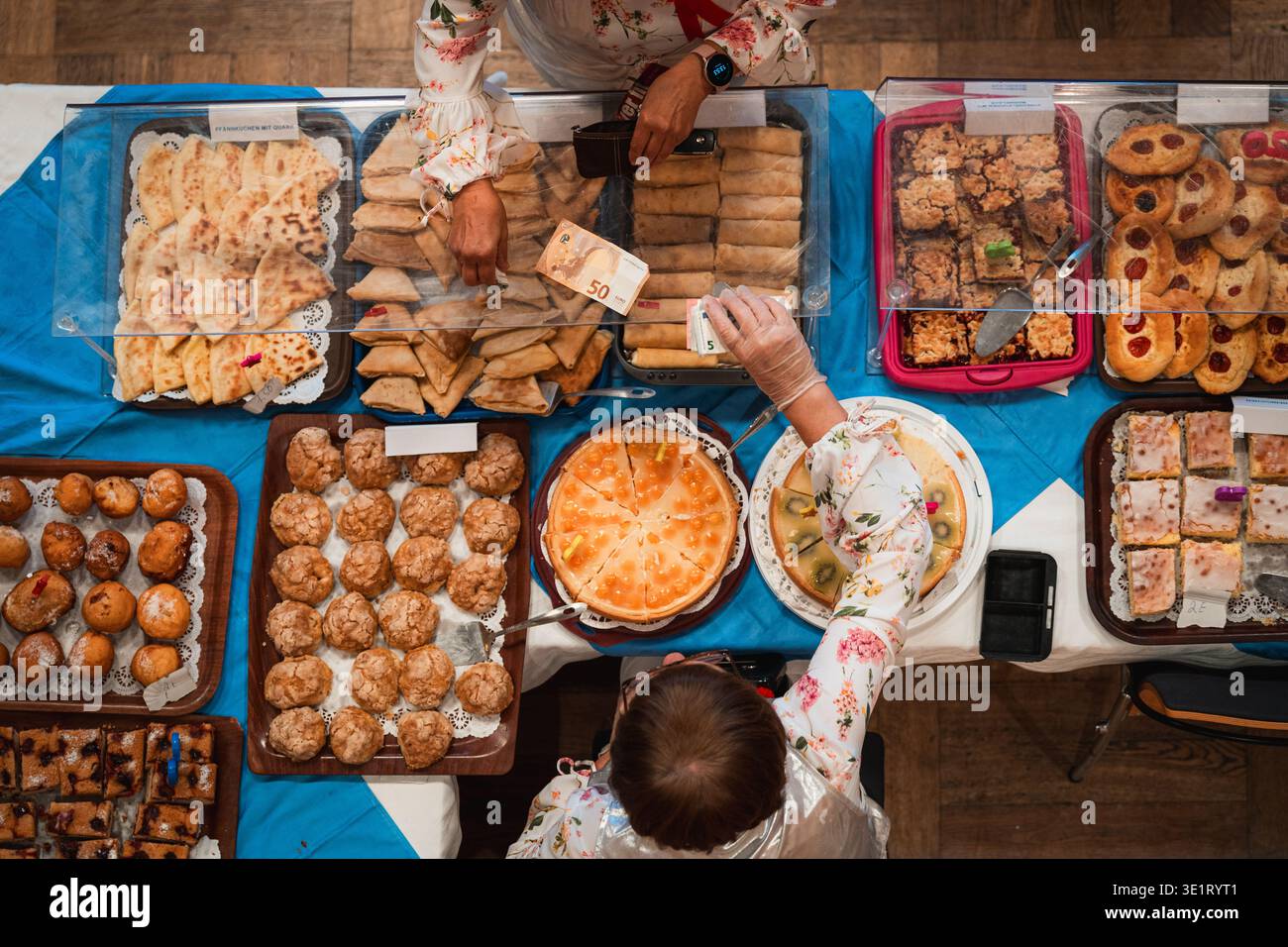Vue de haut en bas d'un étal de marché très fréquenté présentant un assortiment de pâtisseries, gâteaux et produits de boulangerie pendant que les clients échangent de l'argent Banque D'Images