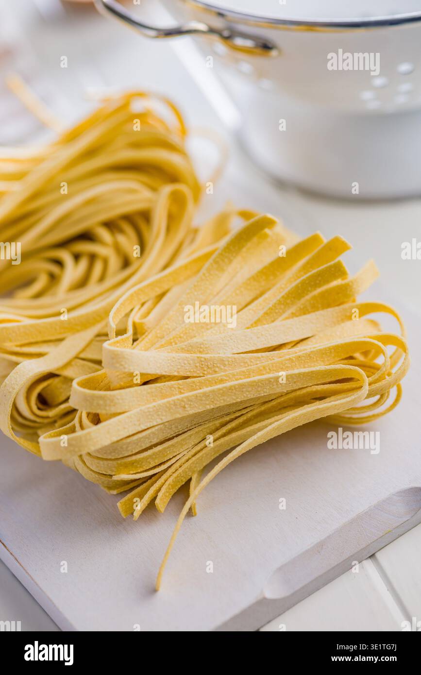 Les brins de pâtes fettuccine reposent sur une surface blanche, paraissant doux et frais. Ce type de pâtes est souvent utilisé dans divers plats. Banque D'Images