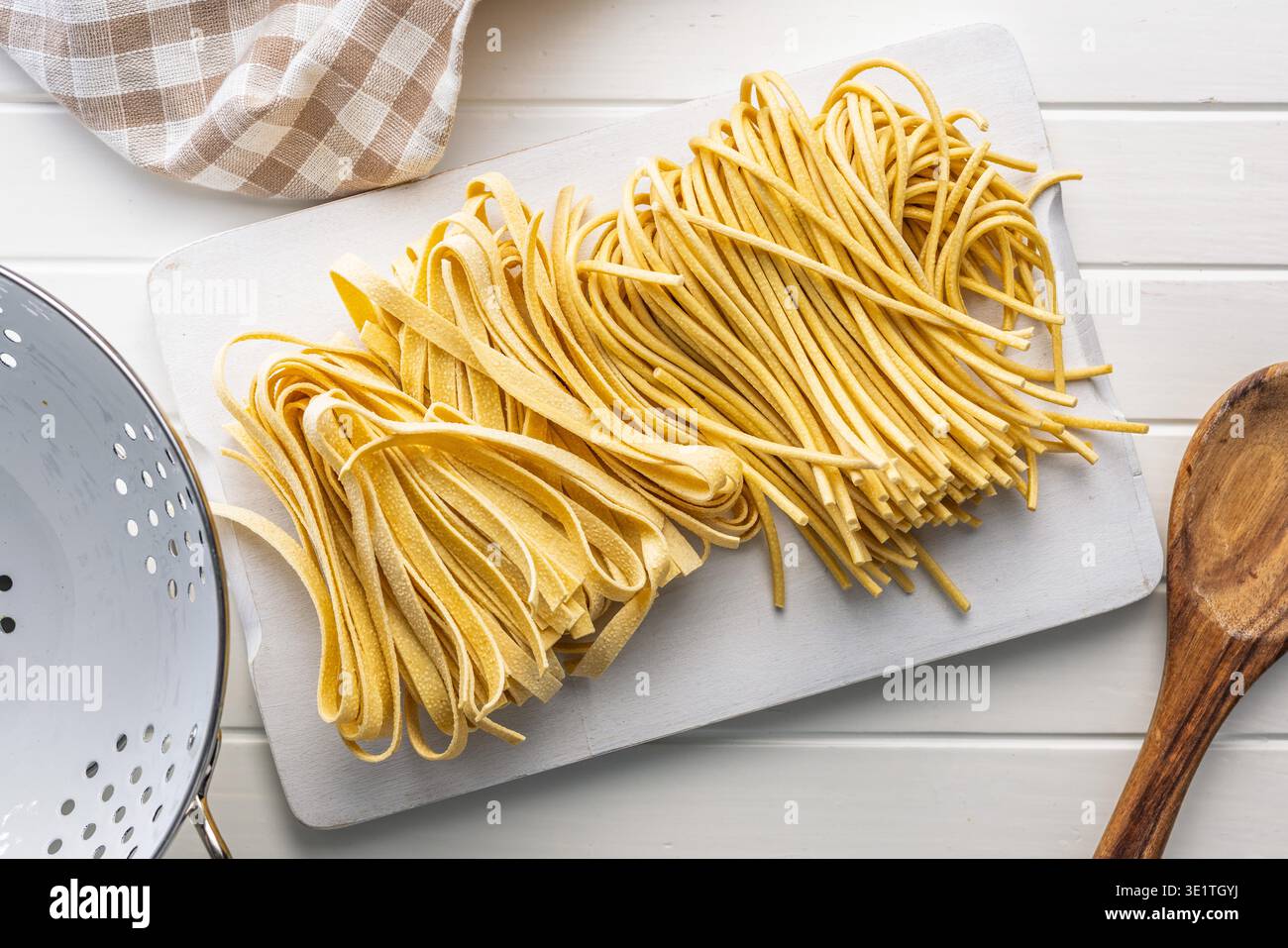 Des brins de fettuccine et de bigoli reposent sur une surface blanche, paraissant doux et frais. Ce type de pâtes est souvent utilisé dans divers plats. Banque D'Images