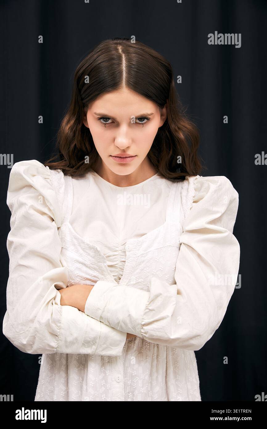 Jeune femme élégante dans une tenue élégante transmet une présence émotionnelle puissante sur un fond sombre. Banque D'Images