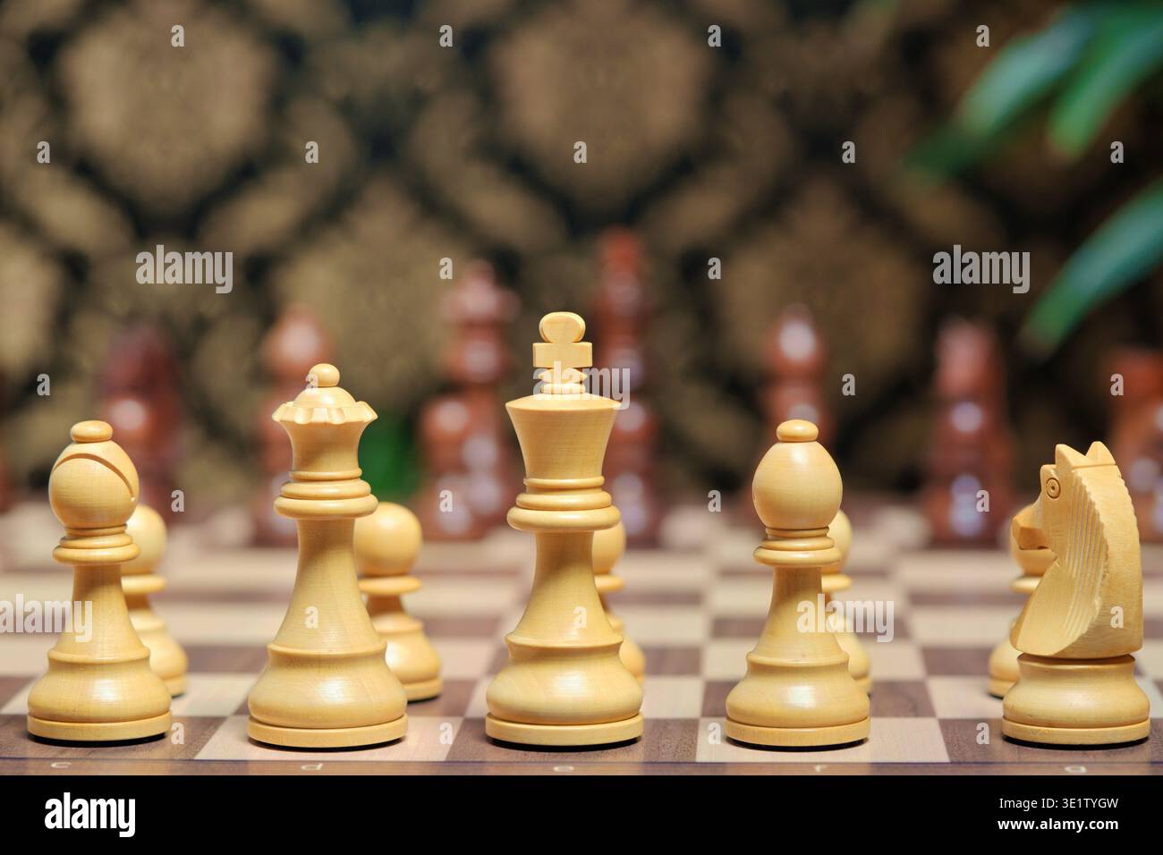 Pièces d'échecs en bois blanc sur un échiquier. Roi, reine, et évêque dans le focus. Arrière-plan flou avec papier peint à motifs. Stratégie et concept de jeu Banque D'Images