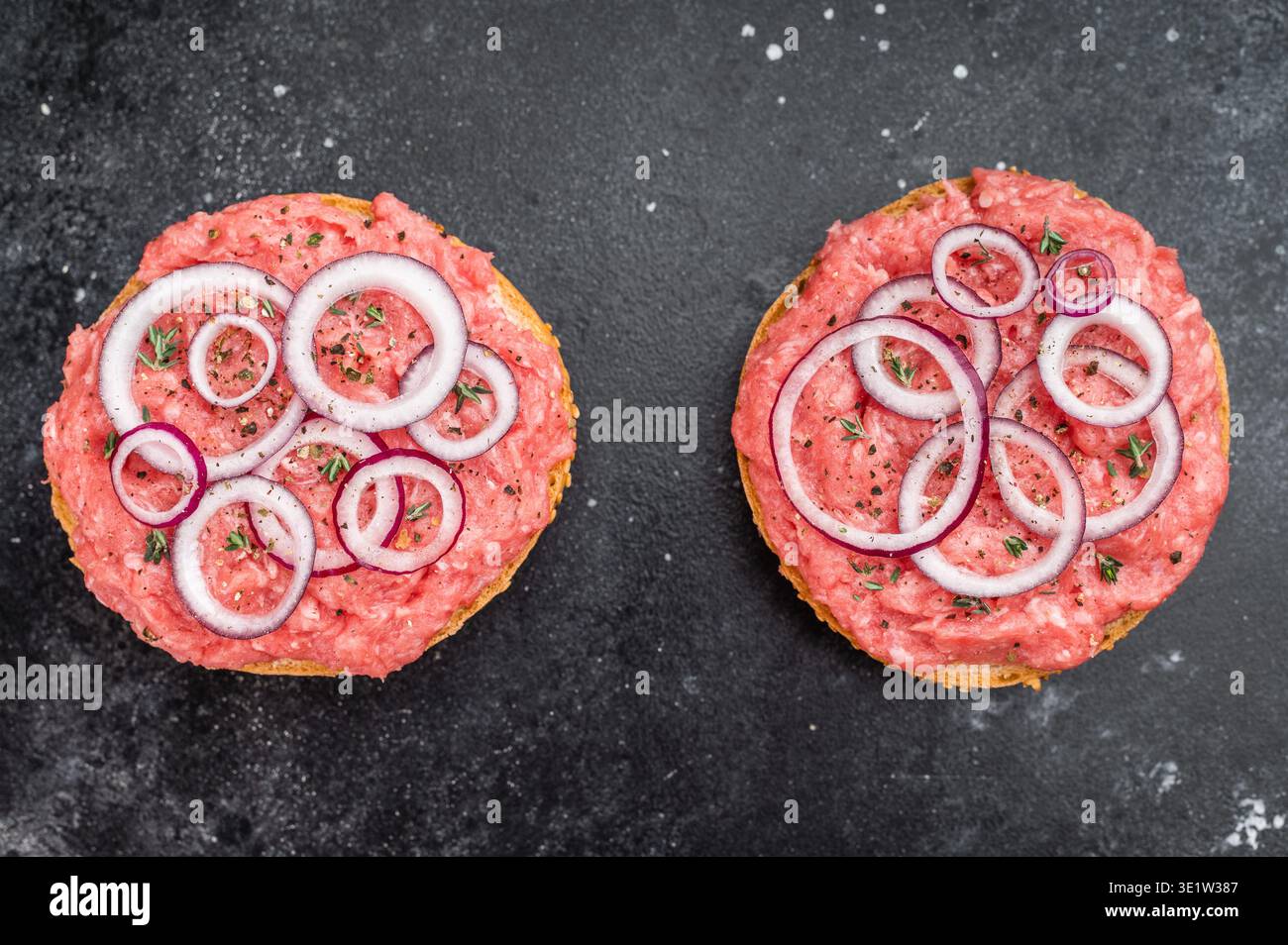 Mettbroetchen sandwichs de porc allemand avec porc haché cru étaler les rondelles d'oignon et les herbes sur une plaque noire. Banque D'Images