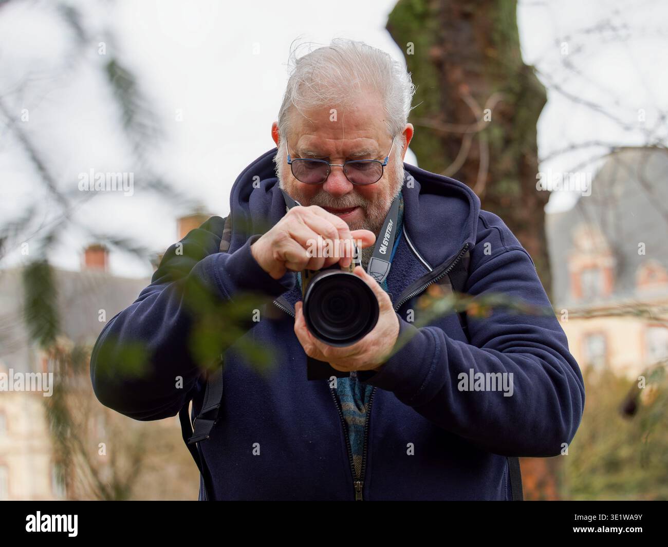 Homme senior tenant un appareil photo et prenant une photo à l'extérieur dans un cadre naturel. Scène met en évidence la photographie comme un passe-temps et la concentration, idéal fo Banque D'Images