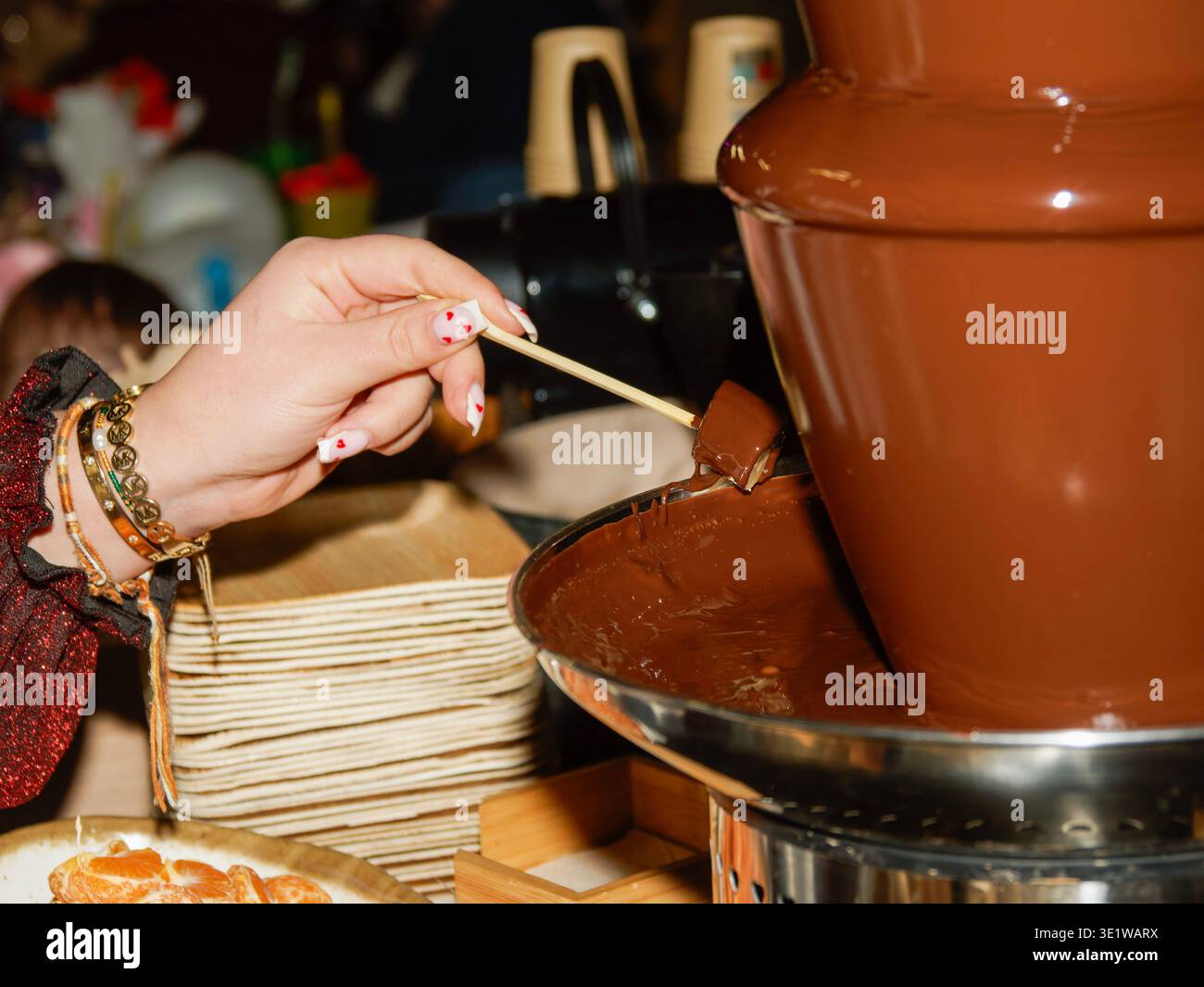 Plonger à la main la nourriture dans une fontaine de chocolat qui coule, parfait pour les buffets de desserts, les fêtes et les événements de restauration avec des friandises sucrées gourmandes. Banque D'Images