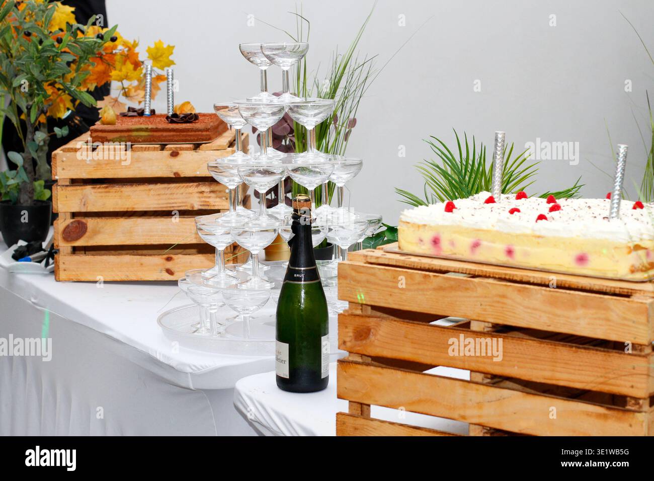Tour de champagne avec verres coupés empilés à côté d'un buffet de desserts et d'un étalage de gâteaux, avec une bouteille de vin mousseux et un décor rustique en bois. Banque D'Images
